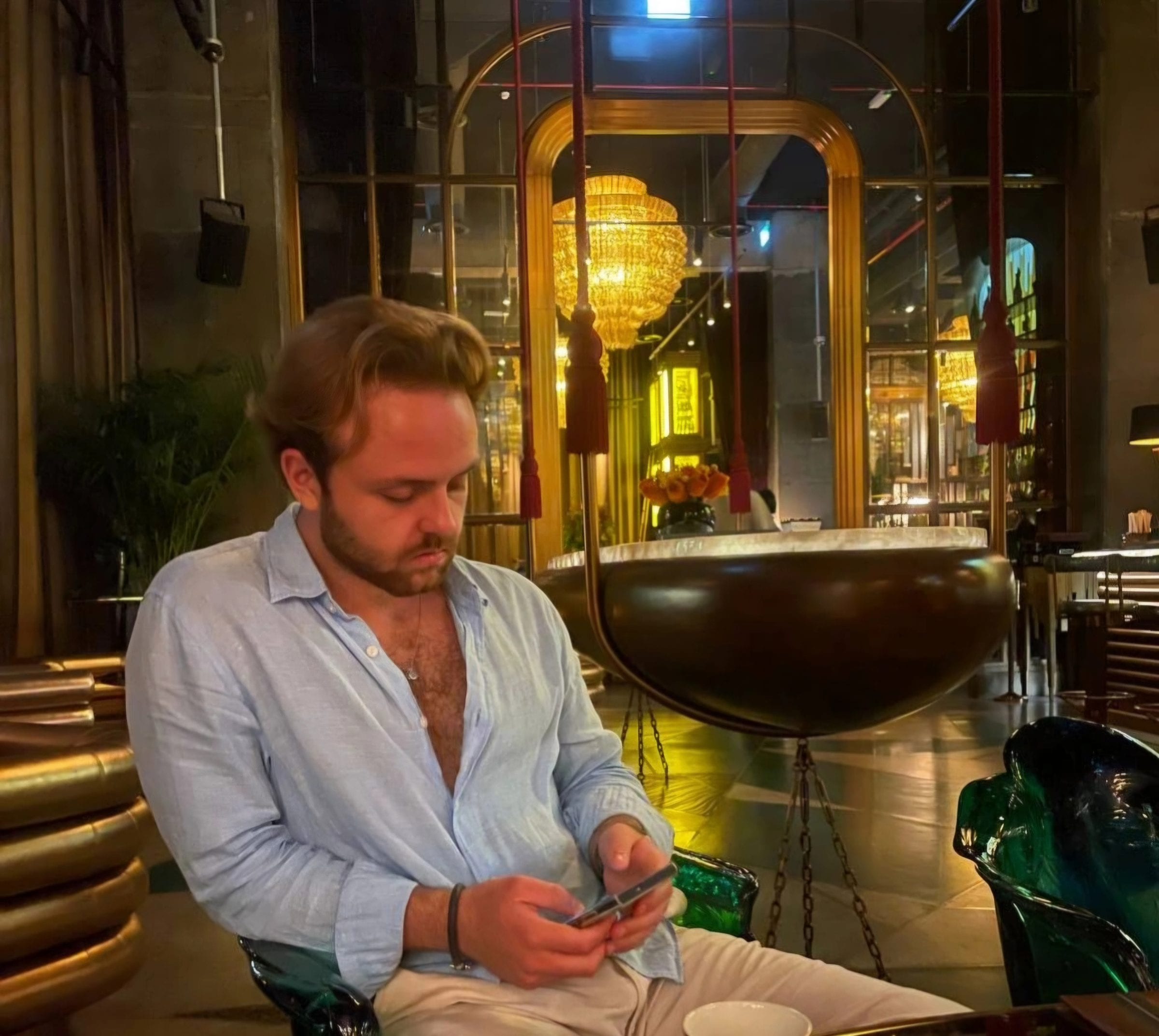 Seated in a hotel lounge in the evening, working from a phone under a chandelier